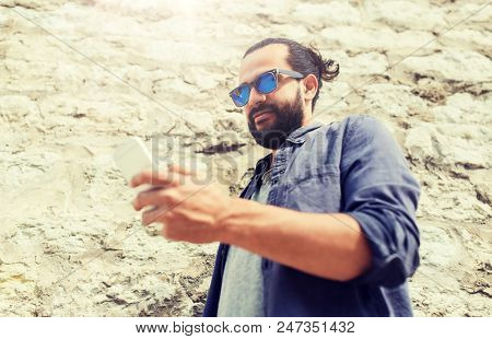 leisure, technology, communication and people concept - man in sunglasses texting message on smartphone at stone wall