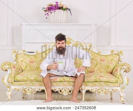 Man With Beard And Mustache Enjoys Morning While Sitting On Luxury Sofa. Man On Sleepy Strict Face I
