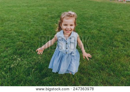 Laughing Little Cute Child Baby Girl In Denim Dress Walking And Running, Have Fun On Green Grass Law