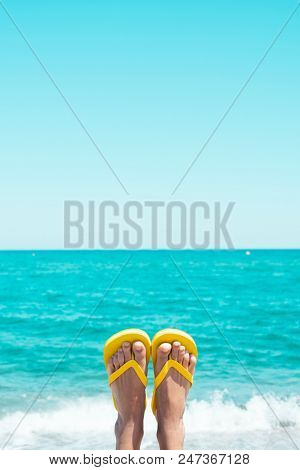 closeup of the legs of a young caucasian man on the beach, upside down, wearing a pair of yellow flip-flops, against the sky with a blank space on top