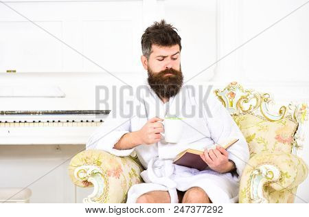 Man With Beard And Mustache Enjoys Morning While Sitting On Luxury Armchair. Man Sleepy In Bathrobe,
