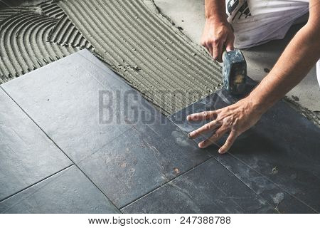 Worker Placing Ceramic Floor Tiles On Adhesive Surface, Leveling With Rubber Hammer