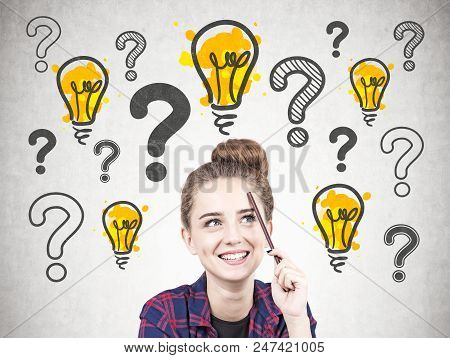 Smiling Hipster Teen Girl With A Pencil Standing Near A Concrete Wall With Many Question Marks And L