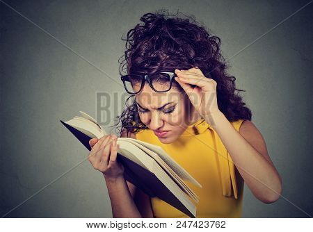 Young Woman With Glasses Reading A Book, Having Difficulties Seeing Text, Has Sight Problems. Eyesig