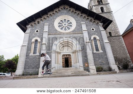 Barcelonnette, France, 8 June 2018: Boy Stunts On Skate Board In Front Of Catholic Church Of Barcelo