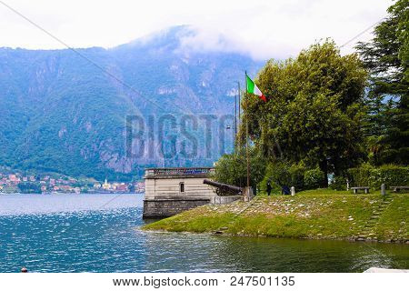 Italian Flag Near Gun With Alps In Background, Lake Como In Mandello Del Lario. Concept Of European 