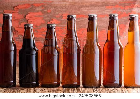 Row Of Seven Types Of Beer In Different Shaped Brown Unlabelled Bottles Against A Rustic Wood Backgr