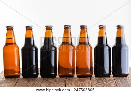 Row Of Dark And Light Unlabelled Bottles Of Homemade Craft Beer On A Rustic Wood Table Against A Whi