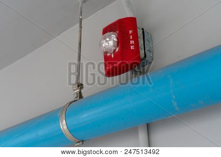 Red Fire Alarm Lighting Above Blue Pvc Pipe Against White Background