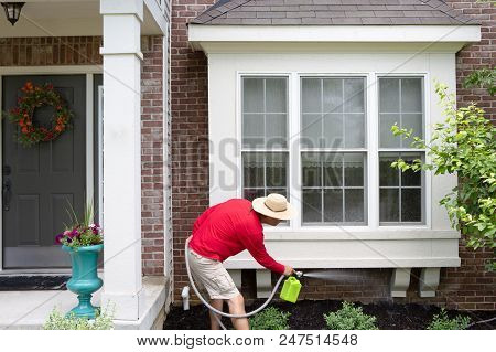 Man Cleaning The Underside Of A Bay Or Bump-out Window On An Upmarket Brick Home Using A Portable Ha