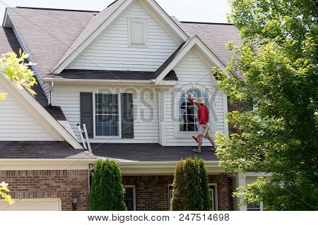 Window Cleaner Cleaning A Large Arched View Window On The Second Floor Facade Of A House Standing On