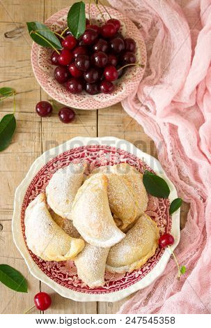 Pies With Cherries, Sprinkled With Powdered Sugar And Berries Of Fresh Cherries On A Wooden Surface.