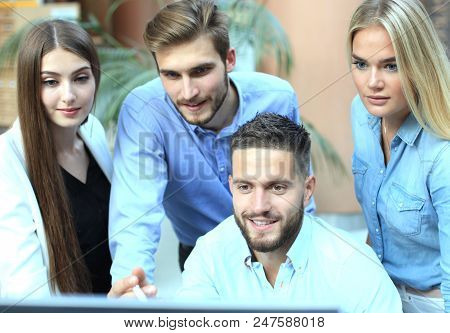 Group Of Young People In Casual Wear Sitting At The Office Desk And Discussing Something While Looki