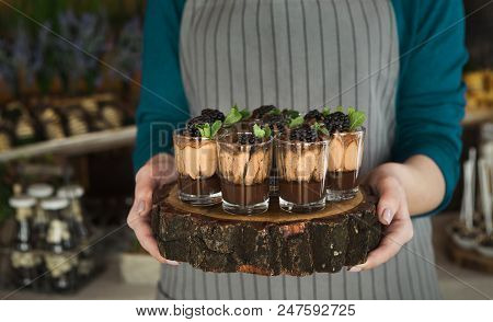 Chef Holding Wooden Tray With Chocolate Dessert Topped With Cream, Blackberry And Mint Leaves In Gla