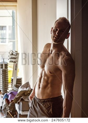 Handsome Muscular Shirtless Young Man Standing In A Gym, Looking At Camera, Leaning On Open Door