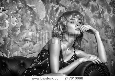 Woman With Thoughtful Expression Sitting On Leather Sofa. Girl In Blond Wig With Nostalgic Look, Mem