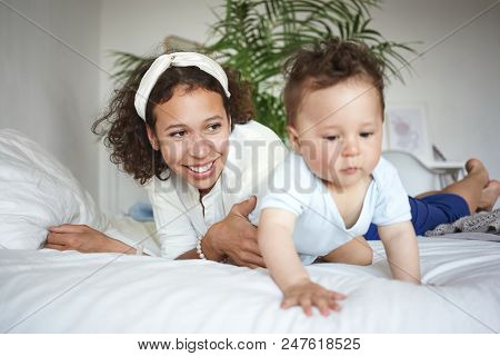 Indoor Shot Of Stylish Happy Young Hispanic Mother Wearing White Headscarf Havig Fun With Adorable C