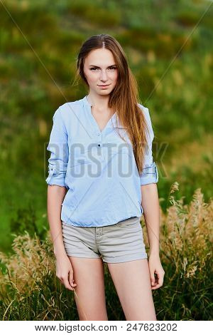 Happy Smiling Young Girl In Blue Shirt And Shorts In The Field