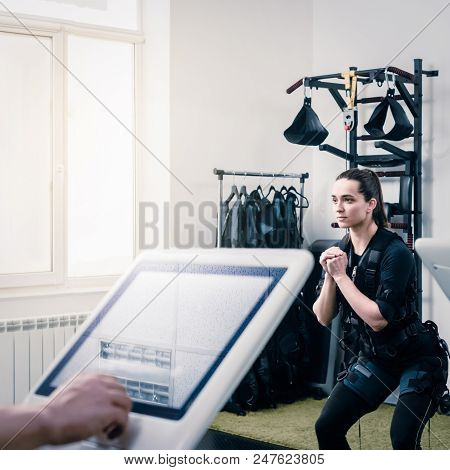 Coach Pushing On Screen On Ems Machine While Woman Waiting For Training, Focus Is On Woman