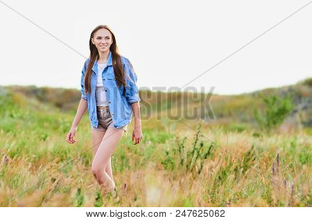 Happy Smiling Young Girl Wearing Blue Jeans Jacket And Shorts Is Standing In The Field