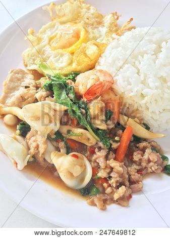 Spicy Fried Basil Leaf And Vegtable With Seafood And Fried Egg With Rice In White Plate On White Bac