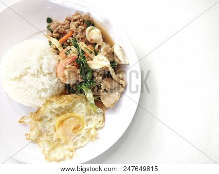 Spicy Fried Basil Leaf And Vegtable With Seafood And Fried Egg With Rice In White Plate On White Bac