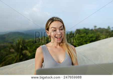 Young Caucasian Female Person Working With Laptop In Green Mountains Background, Wearing Grey Shirt.