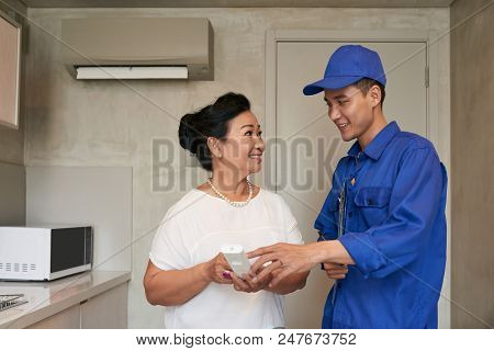 Smiiing Technicial Explaining Vietnamese Senior Woman How To Use Air Conditioner Remote Control