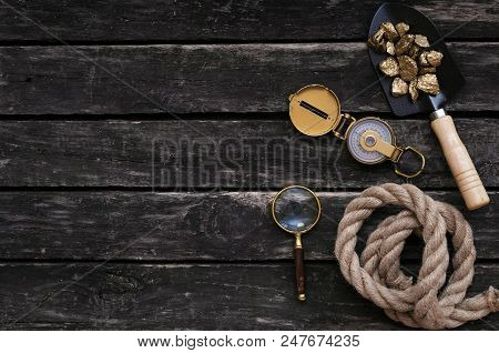 Shovel Full Of Gold Ore, Compass, Rope And Magnifying Glass On Aged Wooden Table Background. Treasur