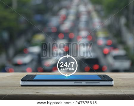 24 Hours Service Icon On Modern Smart Phone Screen On Wooden Table Over Blur Of Rush Hour With Cars 