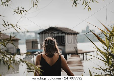 Girl Walking On A Pier In Summer And Got Framed Between Bush And Trees. Little Floating House Or Cab