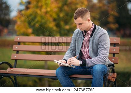 A Cute Student Writes Down His Thoughts In His Notebool Using A Pensil.