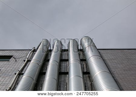 Metal Ducts Attached To Side Of Drab Building On Smoggy Day
