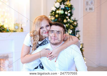 Young Woman Hugging Husband Near Christmas Tree. Concept Of Happy Couple And New Year Atmospehere.