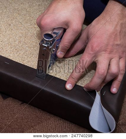 Hands Fastening Brown Leatherette To The Particle Board Using Stapler And Staples