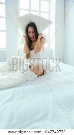 Young caucasian woman covering her head and ears with pillows.