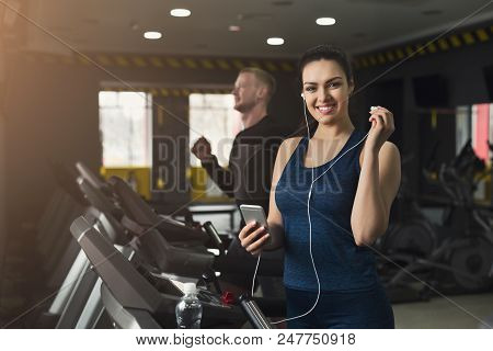 Young Woman With Smartphone Running On Treadmill In Gym. Slim Girl Jogging In Fitness Club, Listen M