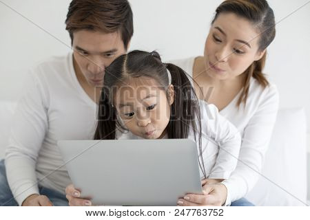 Attractive Little Girl Using Laptop With Mom And Dad Together. Girl Learning To Use Laptop. Happy Fa