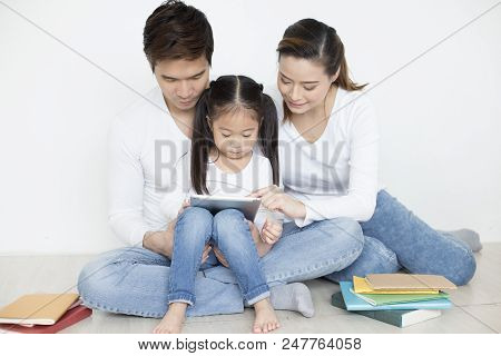 Little Girl Using Tablet With Dad And Mon Together At Home. People With Technology Concept.