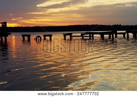 Wooden Pier Or Jetty Remains On Warm Lake Sunset And Sky Reflection Water. Poland.