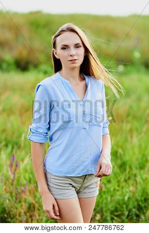 Happy Smiling Young Girl In Blue Shirt And Shorts In The Field