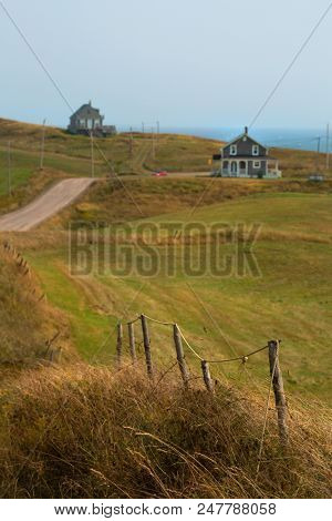 Wooden fence in the field and  few coloured house in Magalen island in Quebec in Canada