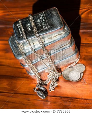 A Stack Of Cast Silver Bars Of Different Weight, Various Silver Coins And Jewelry On A Background Of