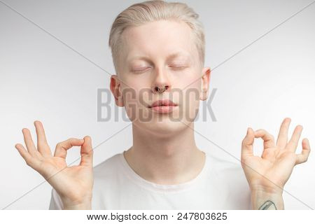 Concentrated Blonde Male Yoga Instructor Having Calm And Peaceful Look, Holding Fingers In Mudra And