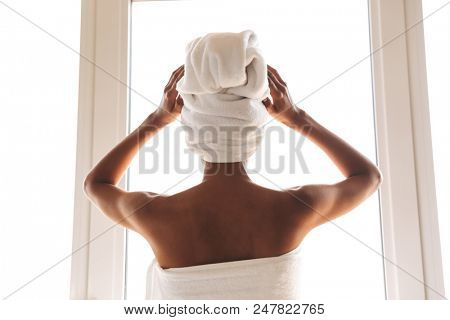 Back view of a young african woman wrapped in a towel standing in front of the wondow