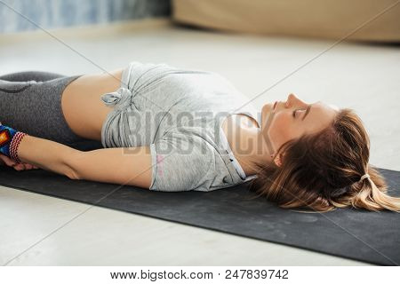 Attractive Young Woman Working Out At Home, Doing Yoga Exercise On Blue Mat, Lying In Shavasana Corp