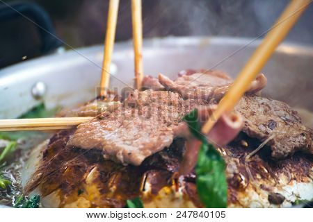 People cooking meat and grill. Food are vegeteble. People use chopsticks.