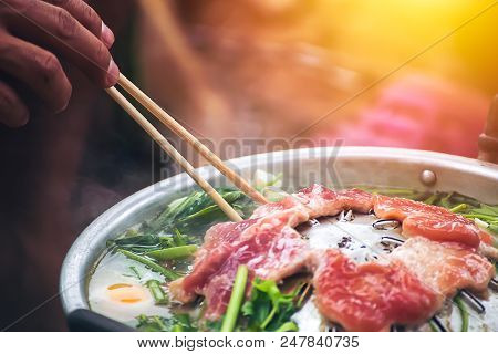 People cooking meat and grill. Food are vegeteble. People use chopsticks.
