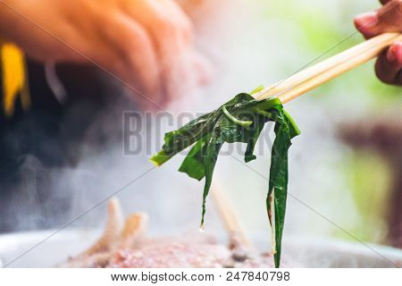 People cooking meat and grill. Food are vegeteble. People use chopsticks.