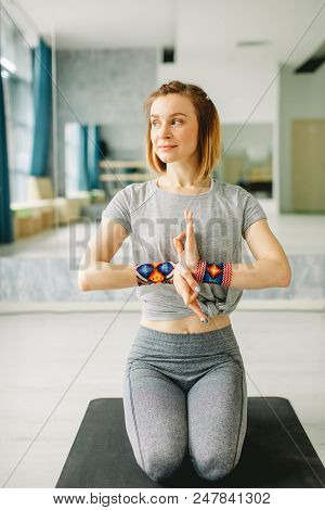 Adult Serene Fit Woman Sitting On Knees With Clasped Hands In Yoga Pose On Mat In Empty Hall Full Of
